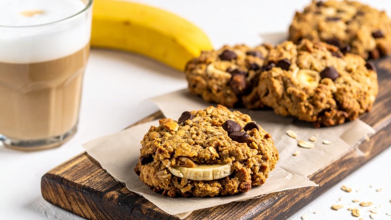 Banana chocolate chip cookies on wooden serving tray alongside whole banana and glass of coffee