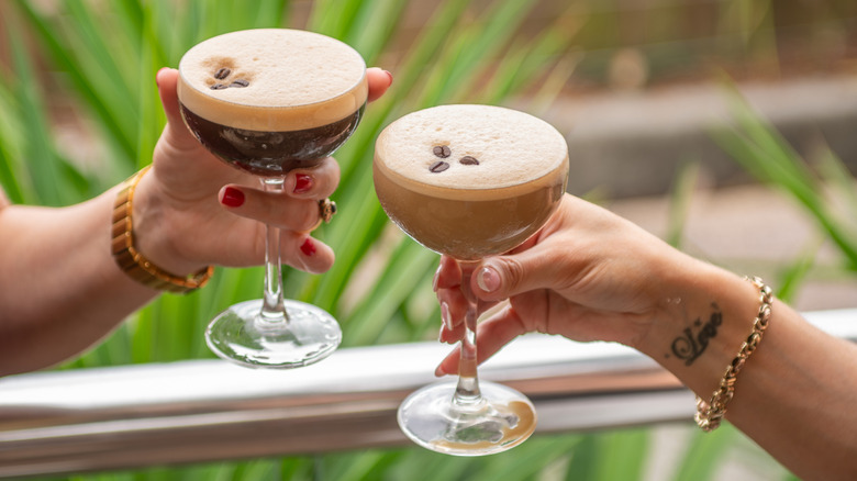 Two hands clinking espresso martini glasses