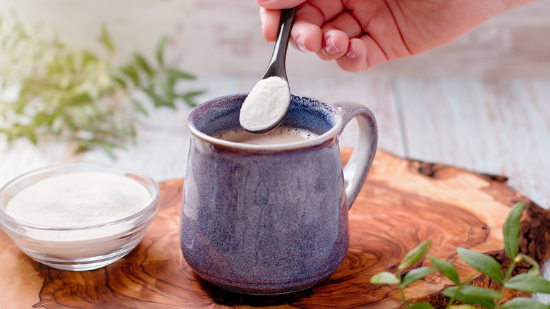 Hand adding spoonful of collagen powder to coffee mug