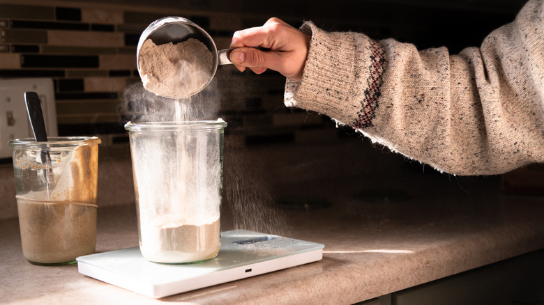 Pouring flour into plastic container to feed sourdough starter