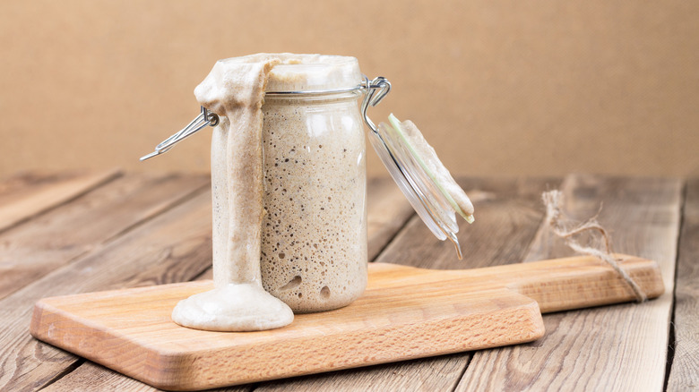 Sourdough starter overflowing from jar onto wood cutting board