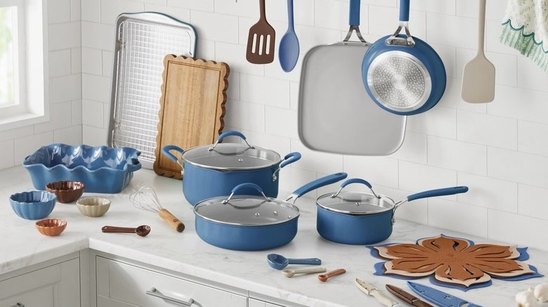 pioneer woman cookware line on a white kitchen countertop surrounded by other spatulas, wooden boards, oven racks, etc.