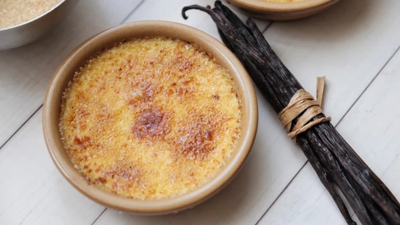 A crème brûlée in a ramekin beside a bundle of vanilla beans