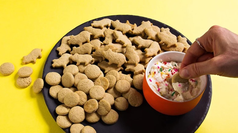 Homemade dunkaroos and a hand dipping them into rainbow sprinkled frosting