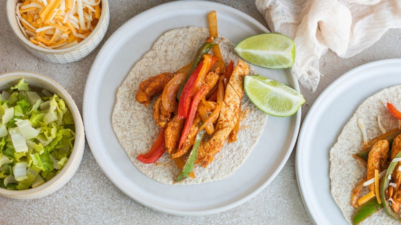 Fajitas on a plate with tortillas, lettuce, cheese, and lime slices