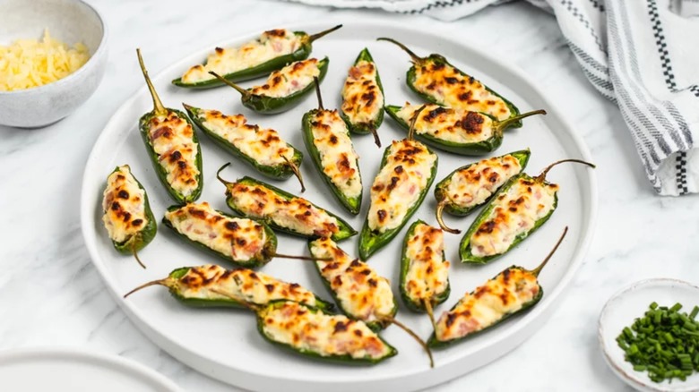 Jalapeño poppers on a plate with shredded cheese and chives on the sid