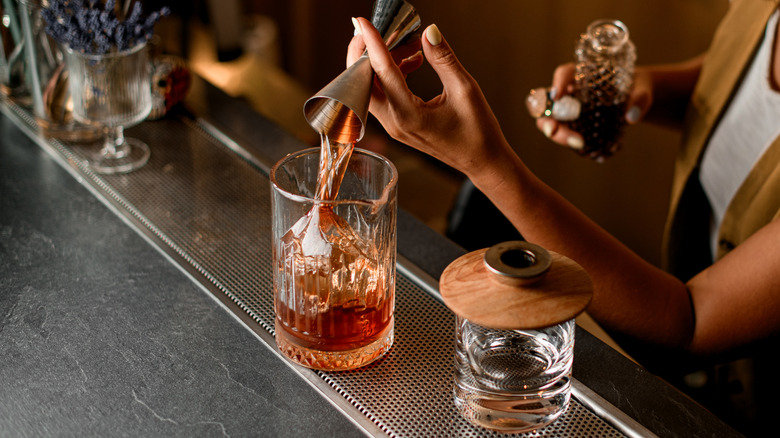 Bartender assembling a cocktail by measuring ingredients with a jigger