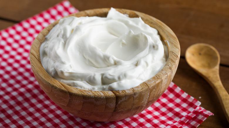 Plain yogurt in wooden bowl on checkered napkin.