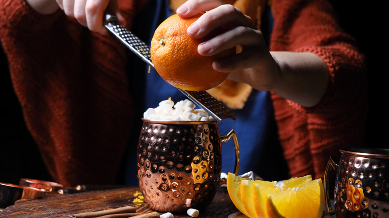 hands zesting orange over mug