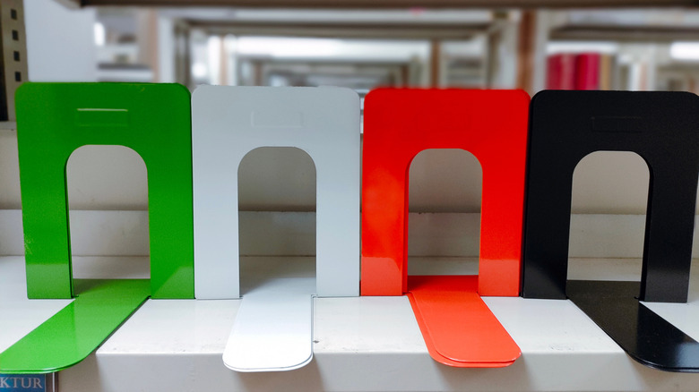 Four simple metal bookends, one green, one white, one orange, one black