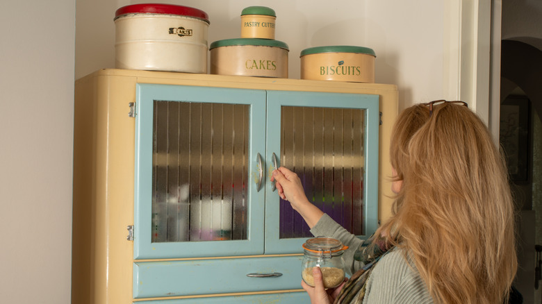 Woman holding jar in one hand and opening blue and yellow larder with the other hand