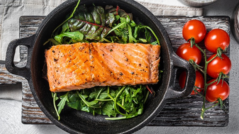 Top-down view of cooked salmon in a skillet with greens and tomatoes