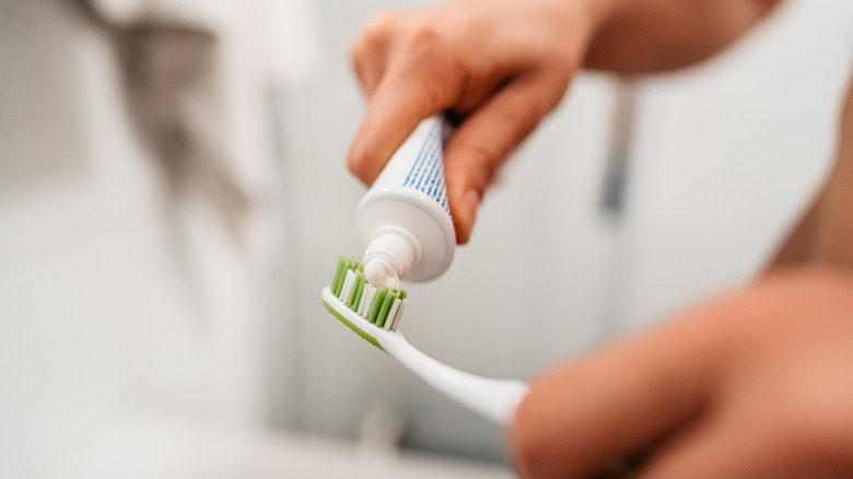 A person squeezing white toothpaste onto a toothbrush