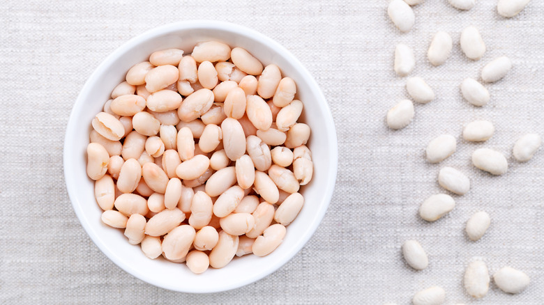 White beans in a wooden bowl next to row of dried beans
