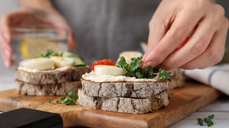 hands stack fresh ingredients on top of bread to make sandwich