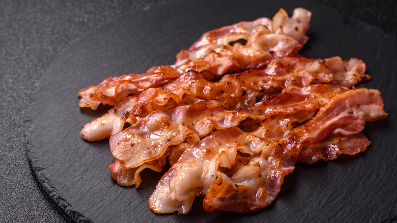 cooked bacon strips on a black slate surface.