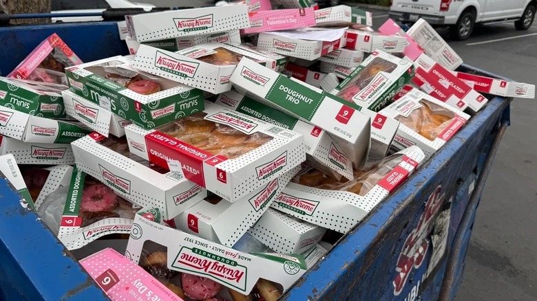 A blue dumpster full of boxes of Krispy Kreme donuts