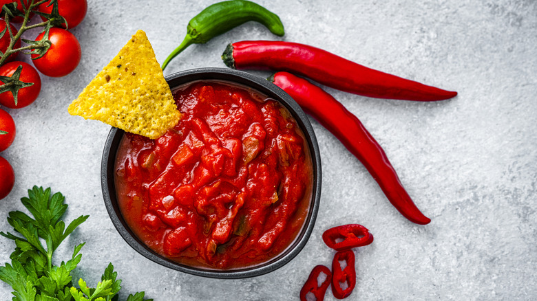 Red chili peppers next to a bowl of salsa with a chip