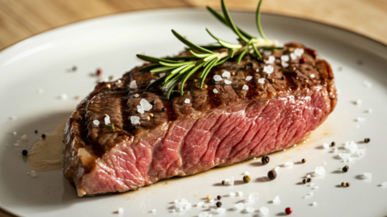 Seared flank steak on a plate with seasoning and rosemary sprig