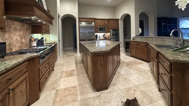kitchen with dark wooden cabinets, granite countertops, clashing tiles and travertine floors