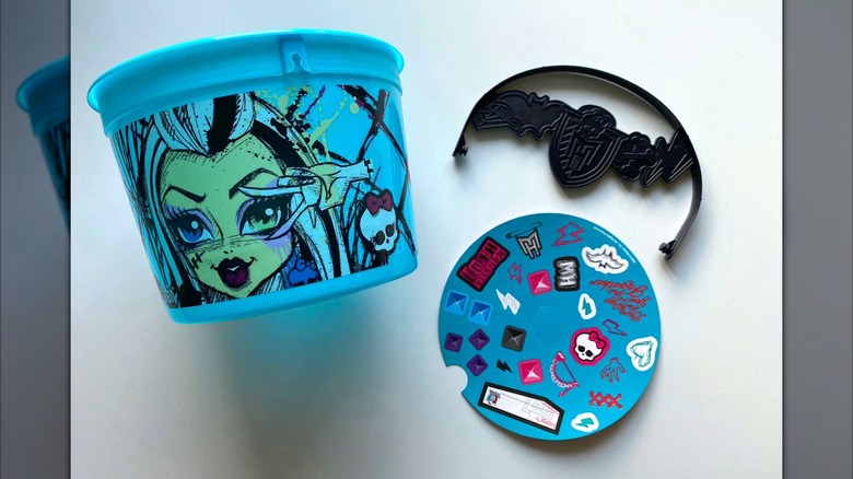 McDonald's blue Monster High Boo Bucket next to sticker sheet on white surface