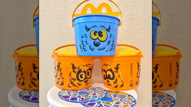 Two orange and one blue McDonald's Boo Buckets next to two sticker sheets