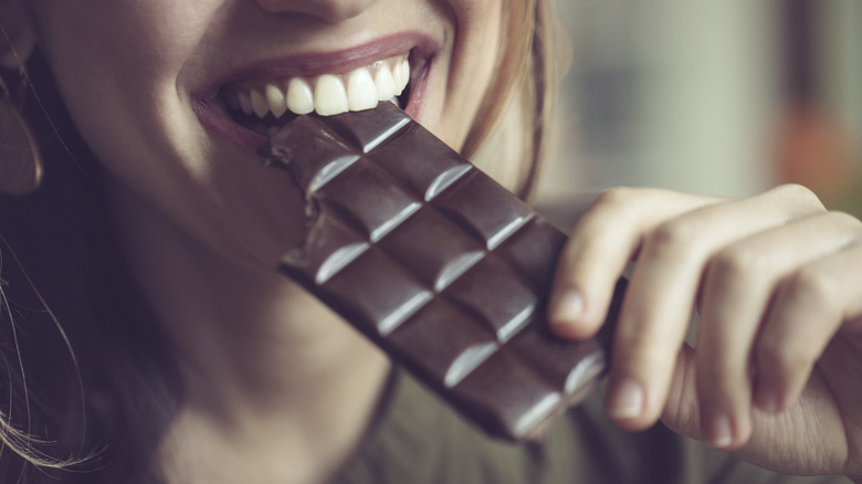 Smiling woman biting into a bar of chocolate