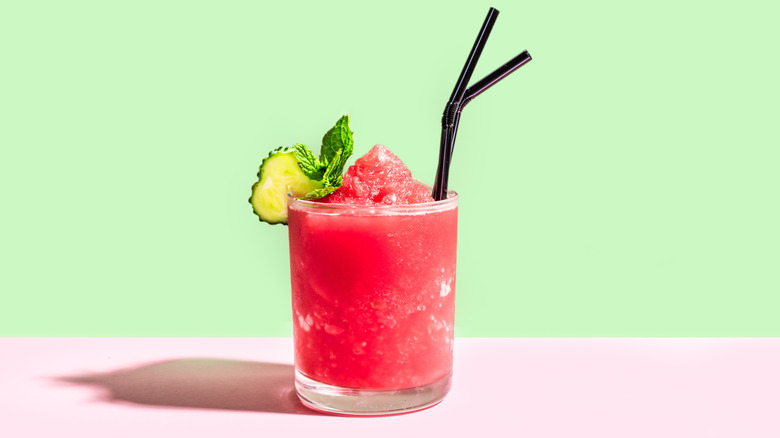 A frozen watermelon slushie with cucumber and mint garnish and two black straws