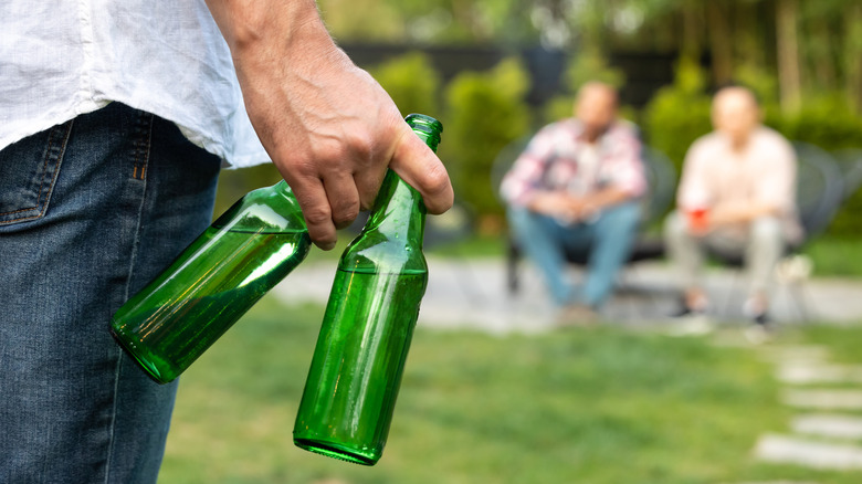 A person holding two green beer bottles approaching two other people who are out of focus in the background