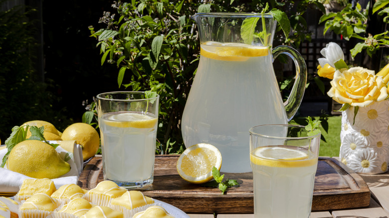 Pitcher of homemade lemonade with lemon on the side, and two glasses filled with lemonade