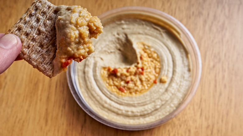 container of roasted red pepper hummus with cracker dipped in