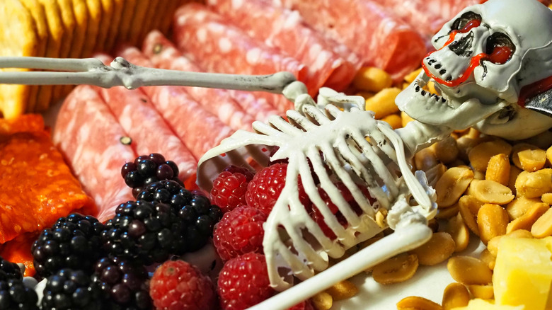 A toy skeleton charcuterie board filled with berries, meat, and cheese