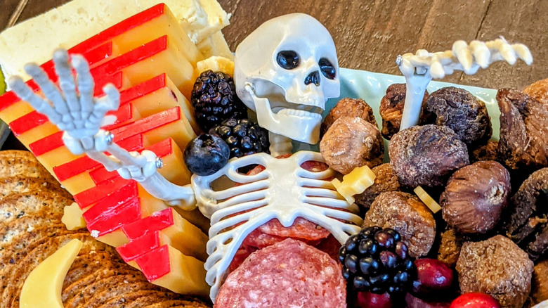 A toy skeleton on a charcuterie board with its arms sticking up