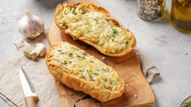 Garlic bread on a cutting board next to garlic cloves