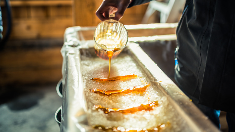 A person pouring maple syrup on snow to make a maple frozen treat