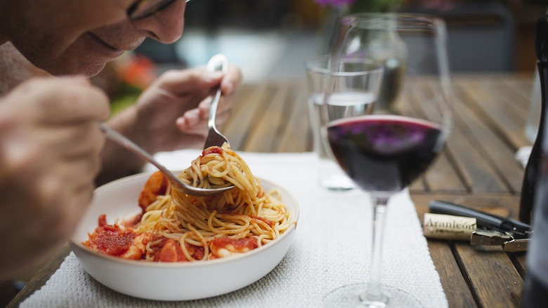 person eating spaghetti with tomato sauce and glass of red wine