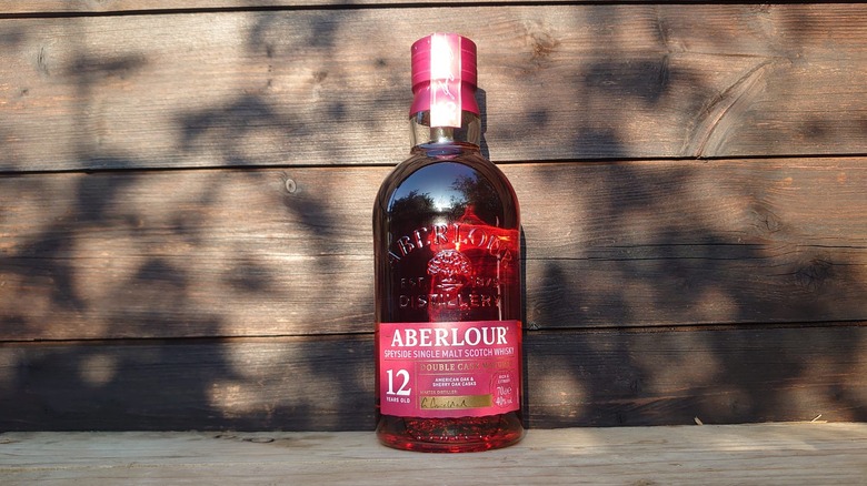 A bottle of Aberlour 12 on its own on a wooden background, showered in dappled sunshine