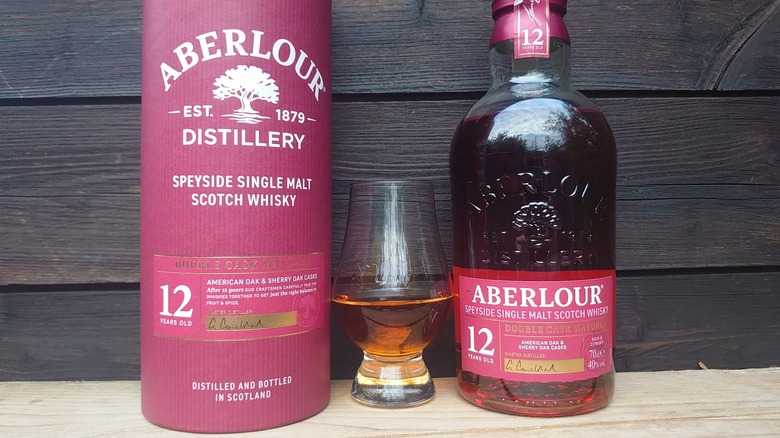 A filled tasting glass of Aberlour 12 with the packaging and bottle either side of a wooden background