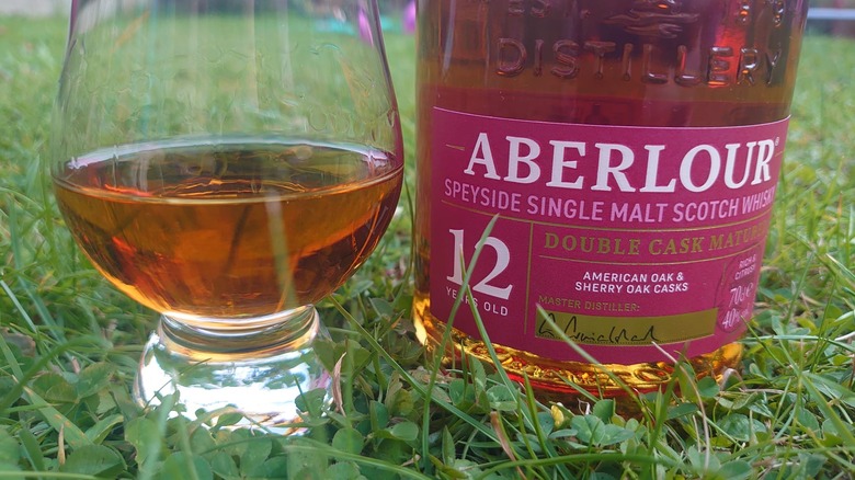 A close up of Aberlour 12 in a tasting glass on grass, with the bottle by its side