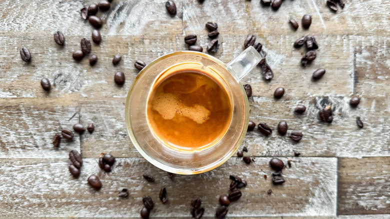 Cup of espresso with beans on wooden surface