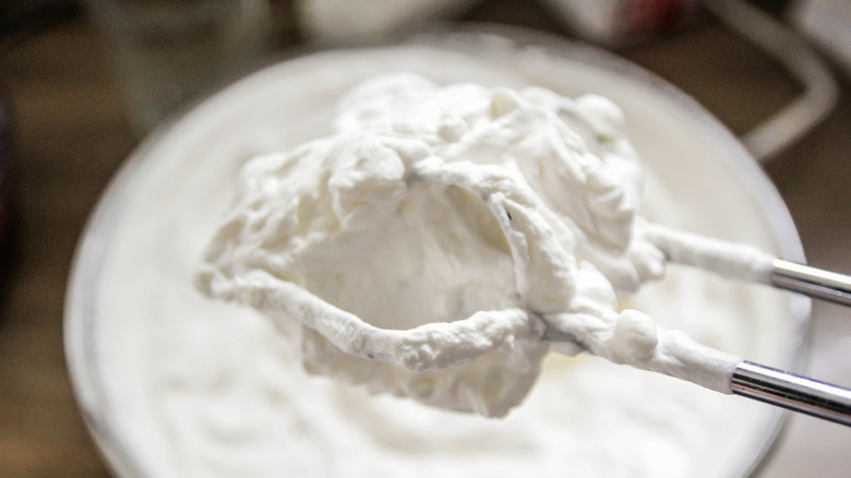 white cake icing on mixer blade above mixing bowl