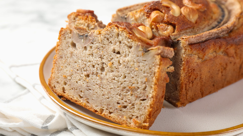 A sliced banana bread topped with nuts sitting on a plate