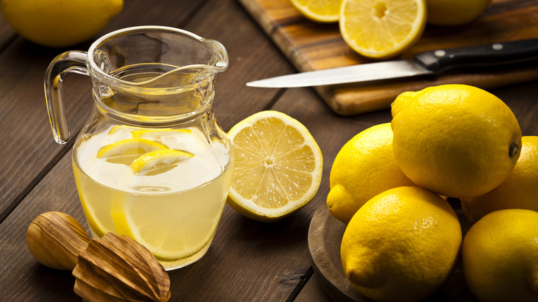 Pitcher of lemonade with lemons, knife, cutting board