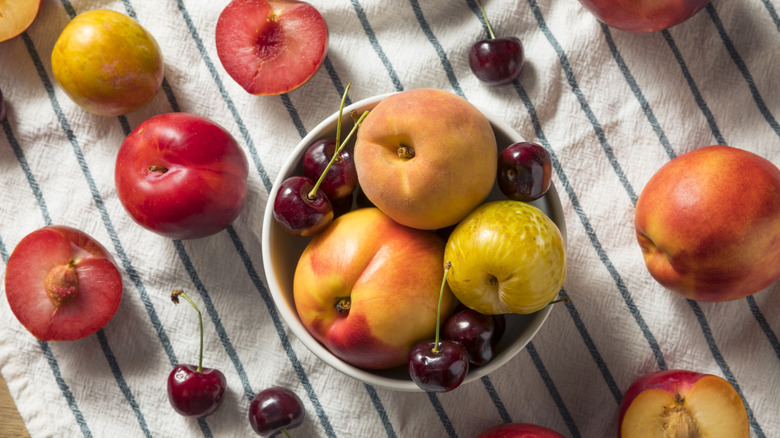 Various stone fruits in a bowl and arranged on a tea towel
