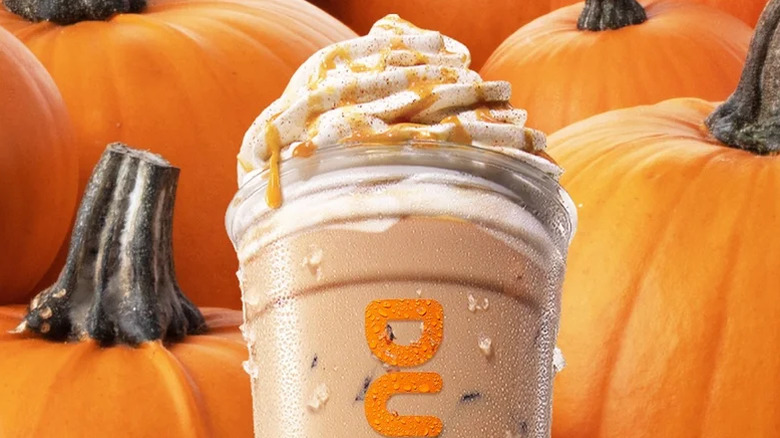 An iced Dunkin' Signature Pumpkin Spice Latte surrounded by pumpkins