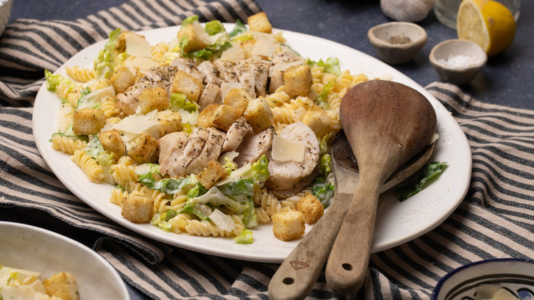 Caesar chicken pasta salad on plate with serving spoons