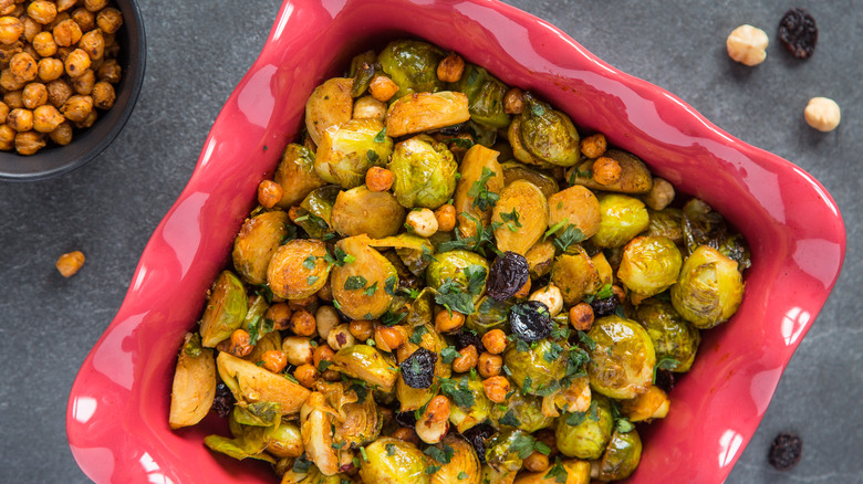 roasted brussels sprouts topped with chickpeas and raisins in a pink serving dish