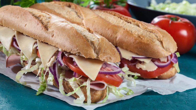 Two Italian sub sandwiches with cheese, onions, lettuce, tomato, and cold cuts