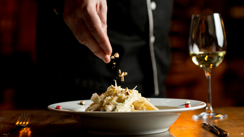 chef sprinkles pasta with hazelnuts