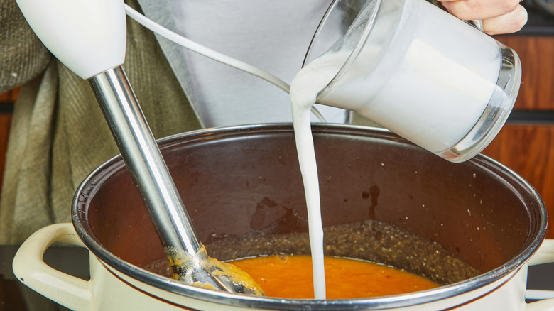 Someone adding cream to a pot of soup, with an immersion blender